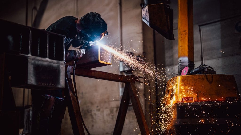 Viser en person som driver med metallbearbeiding ved å sveise et metallstykke. Personen har på seg verneutstyr.