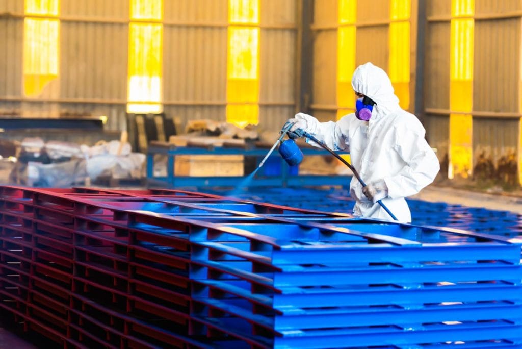 Person i verneutstyr bruker spraymaling til å overflatebehandle metallkonstruksjoner