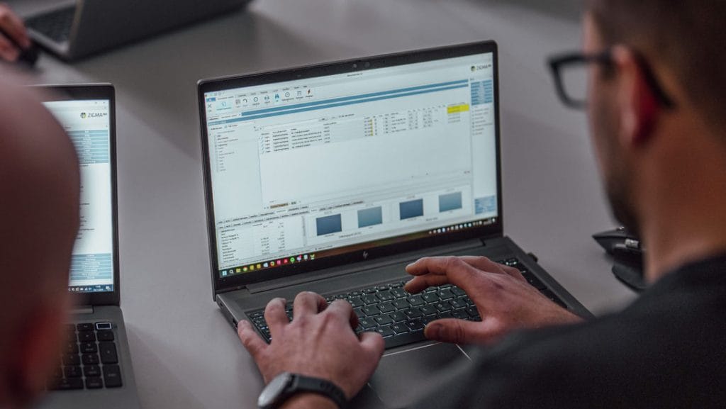 en mann som sitter med ryggen til kamera. Vi ser at han arbeider på en laptop og ser et skjermbilde for ordrestyring og prosjektstyring i Zigma