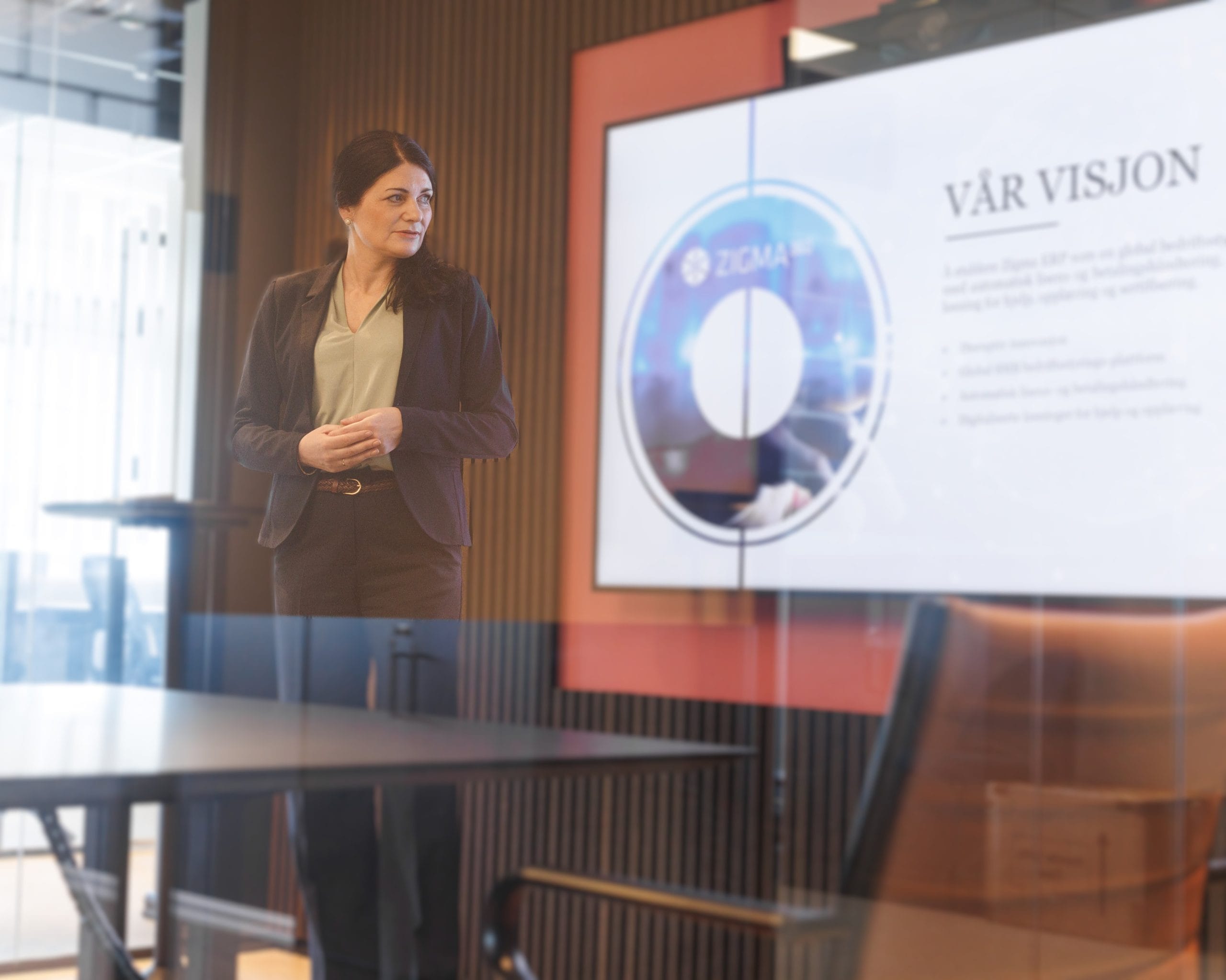 Dame står foran en skjerm i forretningsklær. På skjermen står det "Vår visjon"
