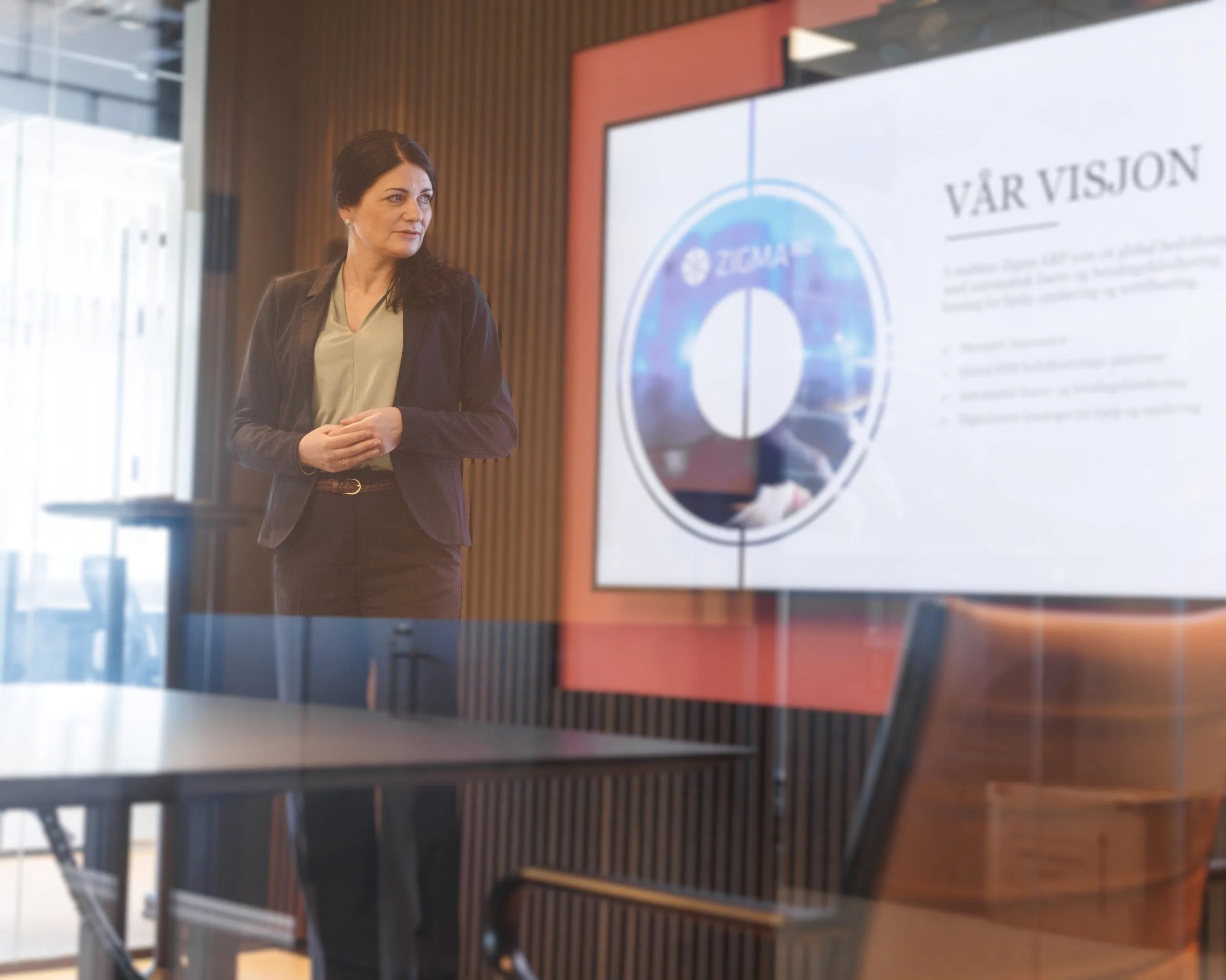 Dame står foran en skjerm i forretningsklær. På skjermen står det "Vår visjon"
